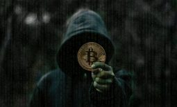 Persona encapuchada sosteniendo una monea con el símbolo de bitcoin