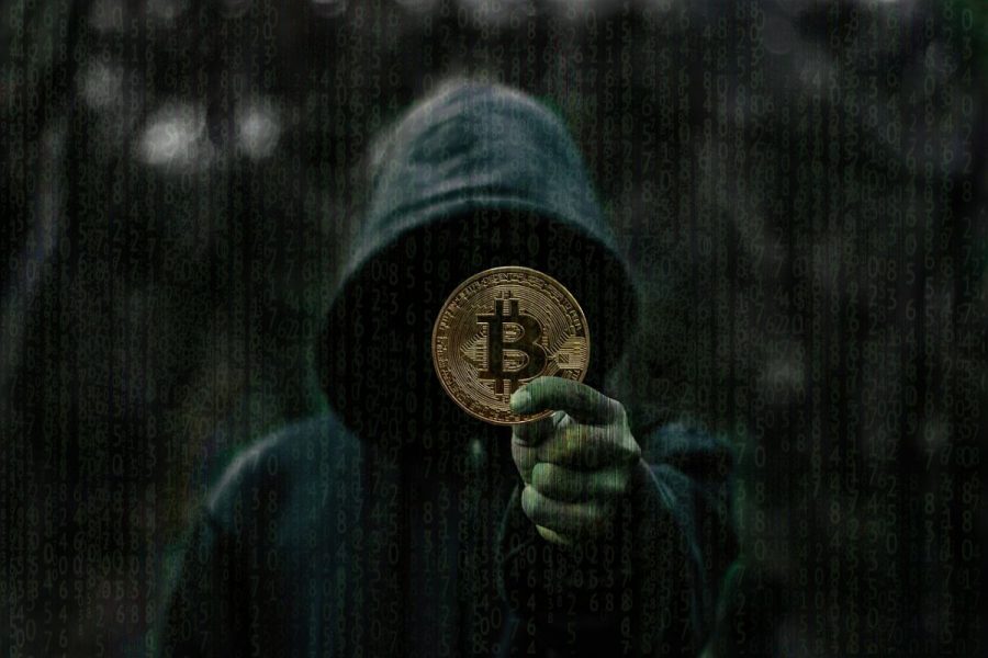 Persona encapuchada sosteniendo una monea con el símbolo de bitcoin